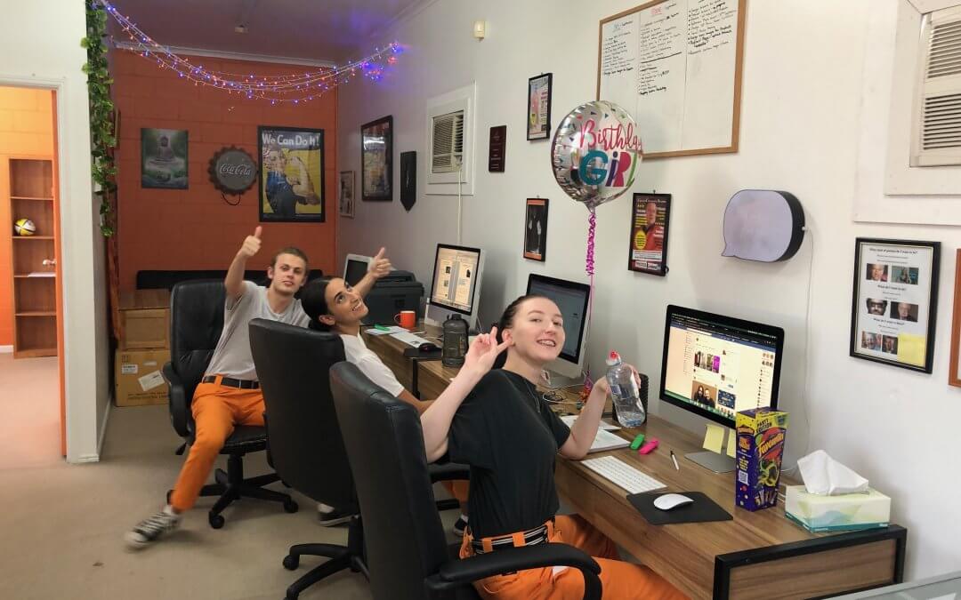 Image of Jessie, Yasmin and Dylan at work sitting at desks waving at camera at Creative Copywriting & Content Solutions Gold Coast